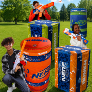 Kids playing behind inflatable Nerf-style bunkers with foam blasters during a backyard battle party.