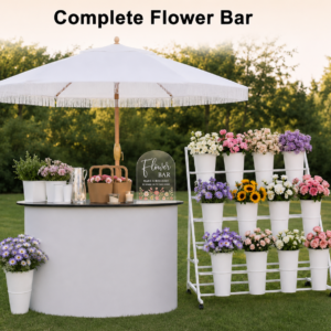 Complete Flower Bar rental setup by Party For Less Rentals in Aurora Colorado with white fringe umbrella, portable counter table, acrylic Flower Bar sign, kraft bags, and 3-tier white display stand filled with colorful flowers for weddings and parties in the Denver area